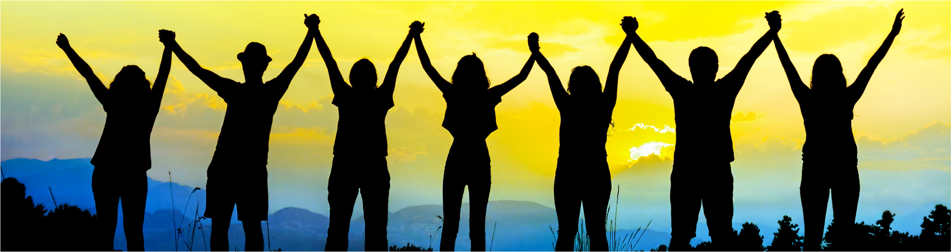 Silhouettes of people holding hands with arms raised, and a view of mountains, clouds, and a yellow sunset in the background